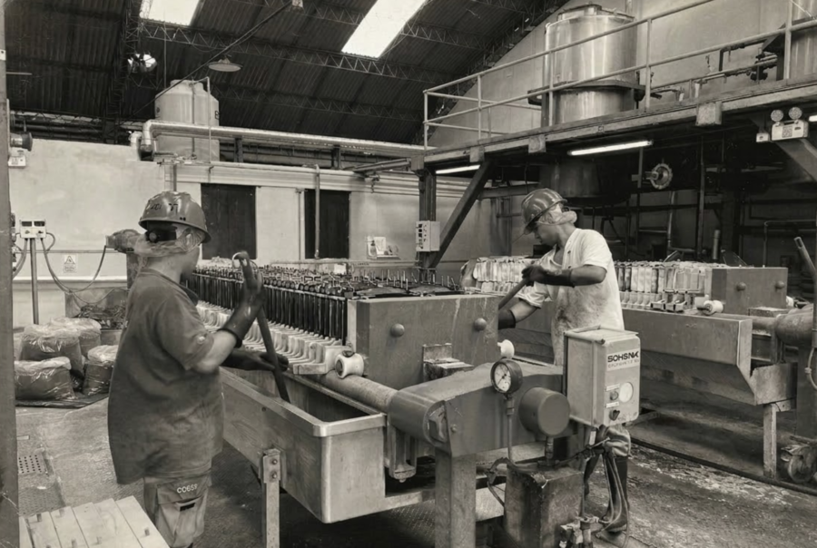 Two skilled BioconColors technicians in professional protective gear operating industrial extraction equipment for natural food colorants in a clean-room factory environment.